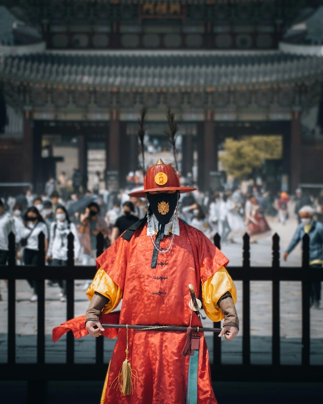 “Traditional guard in red uniform standing at Gyeongbokgung Palace in Seoul during the royal guard changing ceremony.”