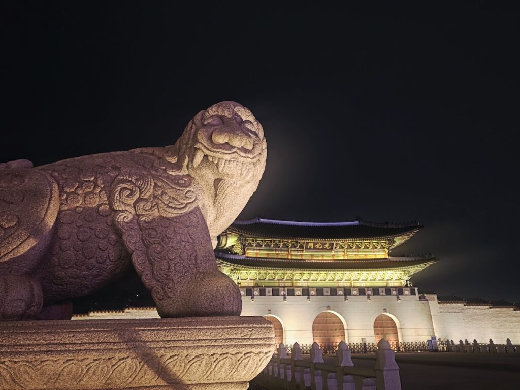 alien-registration-card-arc-korea-guide-gwanghwamun-gatekeeper A dramatic close-up of the mythical Haechi statue at Gwanghwamun Gate in Seoul at night, symbolizing the strict gatekeeping of the Korean social system and the protection unlocked by the Alien Registration Card (ARC) Korea Guide 2026.