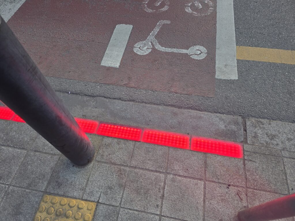 barrier-free-seoul-subway-wide-gate-access A wide, automatic priority gate at a Seoul subway station entrance, specifically designed for wheelchair users and those with strollers. The gate features a prominent blue wheelchair icon and offers ample space for easy passage without stairs.