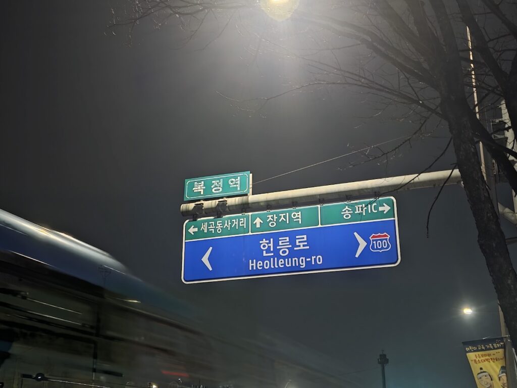 A view of Bokjeong Station Exit 2 at night, showing the active transit hub dynamics with a Seoul city bus (Route 345) and subway signage, establishing it as a strategic location for Gangnam access.