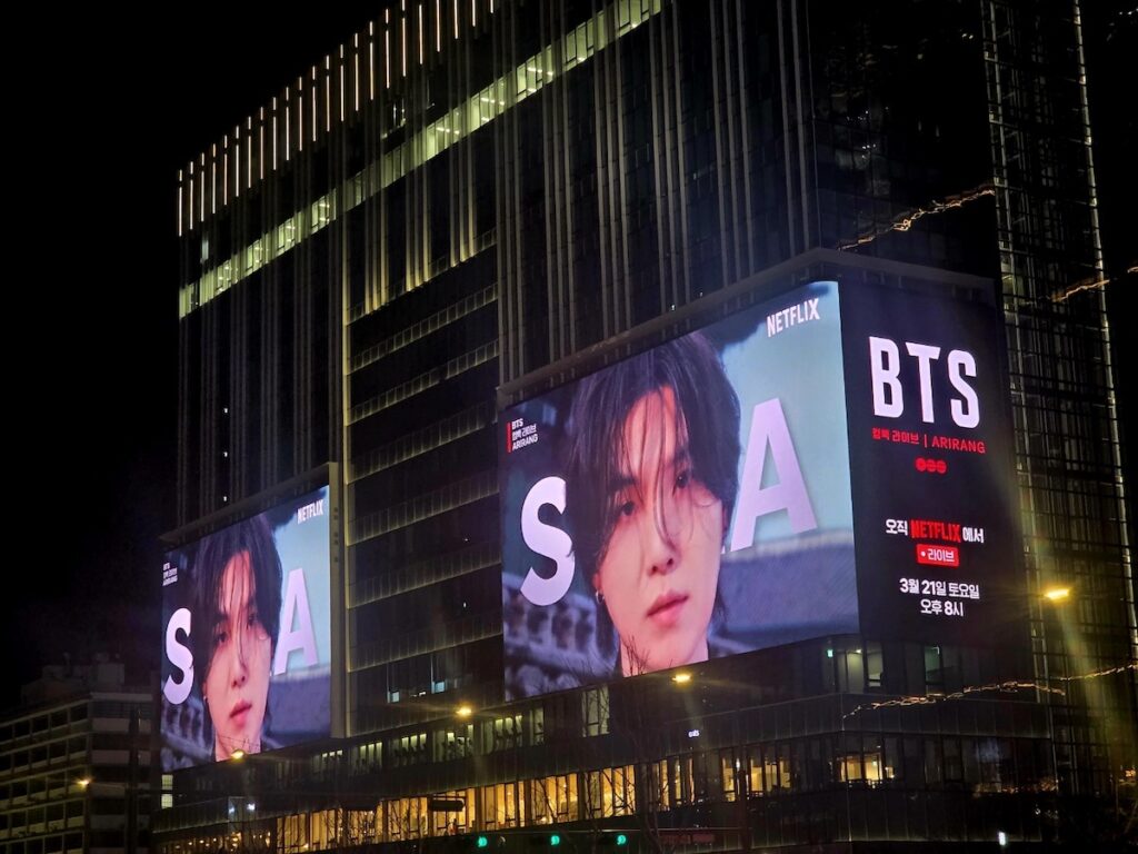 bts-gwanghwamun-traffic-guide-suga-billboard-alerts A glowing BTS billboard at Gwanghwamun. Beyond this vibrant display lies the "Red Line" vehicle exclusion zone as detailed in the BTS Gwanghwamun Traffic Guide 2026.