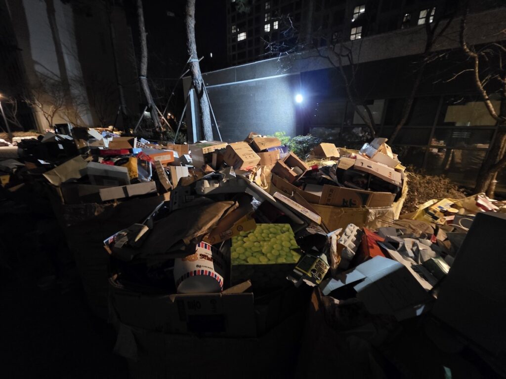 delivery-cardboard-boxes-recycling-in-south-korea-apartment An overwhelming amount of flattened cardboard boxes from online shopping deliveries, organized for collection in a Korean residential area.