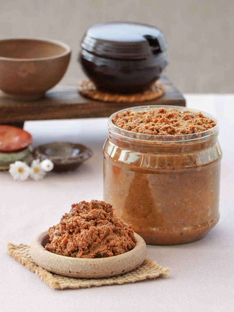 A close-up of traditional Korean doenjang, a thick brown fermented soybean paste served in a small earthenware bowl.