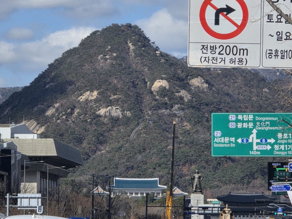 f-2-99-visa-korea-requirements-gwanghwamun-seoul A daytime view of Gwanghwamun square featuring the Admiral Yi Sun-sin statue and the Blue House against Mount Bugaksan, illustrating the solid legal foundation of F-2-99 visa Korea requirements for long-term residents.