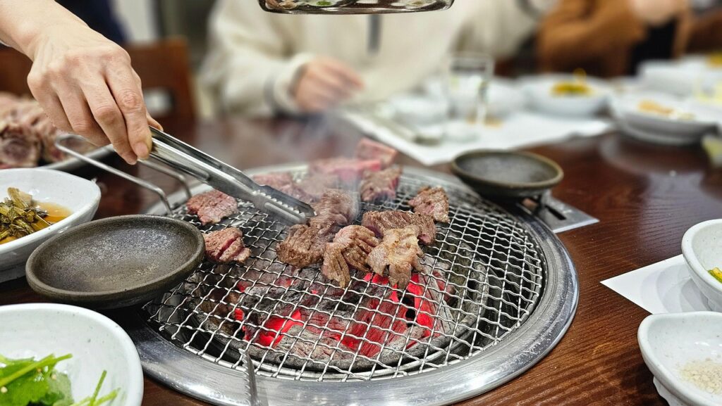 Hanwoo chuck flap tail sizzling on a Korean BBQ grill, with golden-brown edges and gentle smoke rising above the fire.