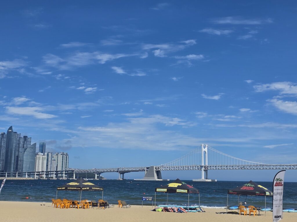 Stand-up paddleboards on Gwangalli Beach sand with Gwangan Bridge and the Busan skyline across the bay