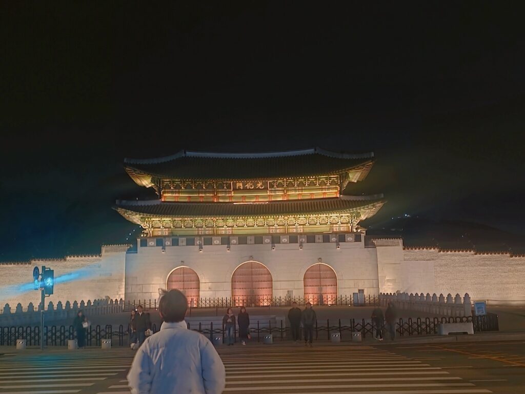 gwanghwamun-gate-night-bts-concert-seoul A high-resolution night photograph of the illuminated Gwanghwamun Gate in Seoul, showing the historic architecture under a dark sky as fans begin to gather for the 2026 BTS comeback concert, symbolizing the intersection of Korea's royal past and its global K-pop future.