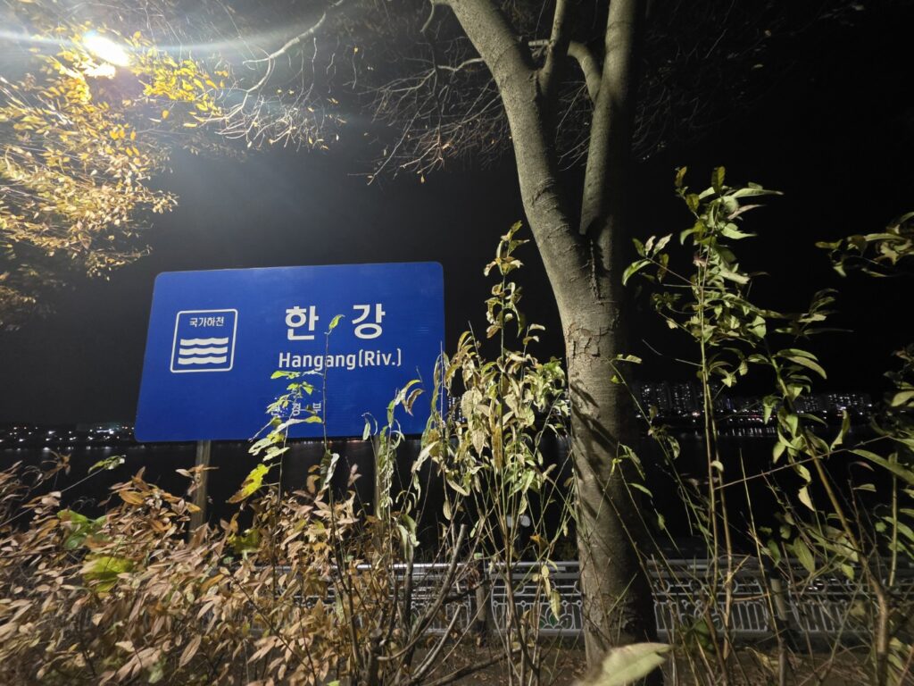 A night view of a Han River signpost near Misa-dong, illuminated by streetlights along the riverside walking path.