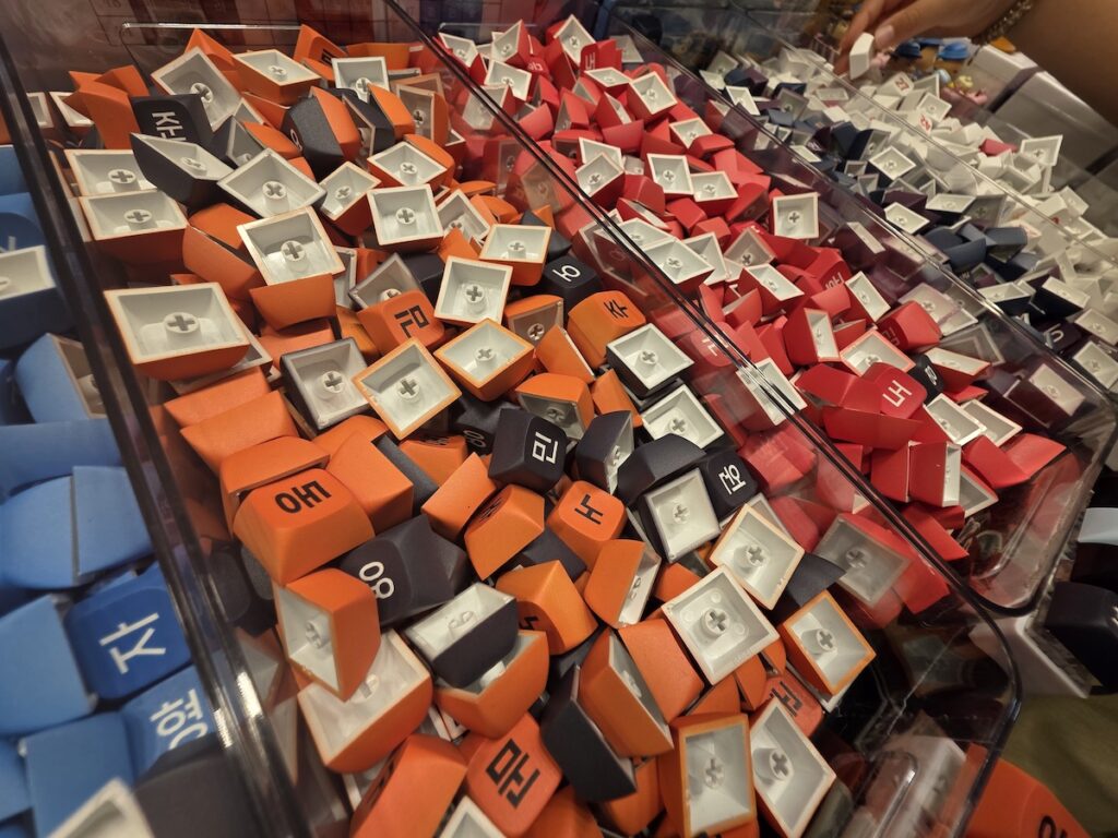 hangul-alphabet-korean-keycap-keyring A container overflowing with small, colorful keyboard keycaps printed with Korean Hangul consonants and vowels for personalized initial nameplates.