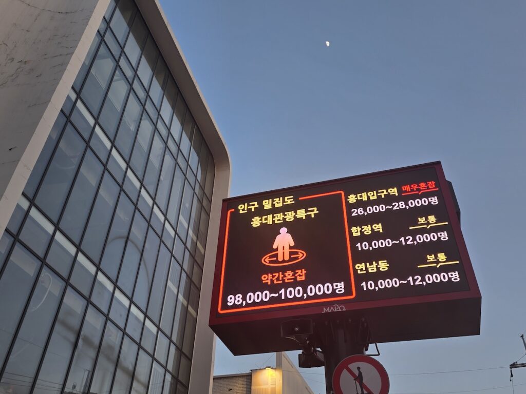 A digital crowd level sign in Hongdae showing visitor density, answering is Hongdae too crowded in real time