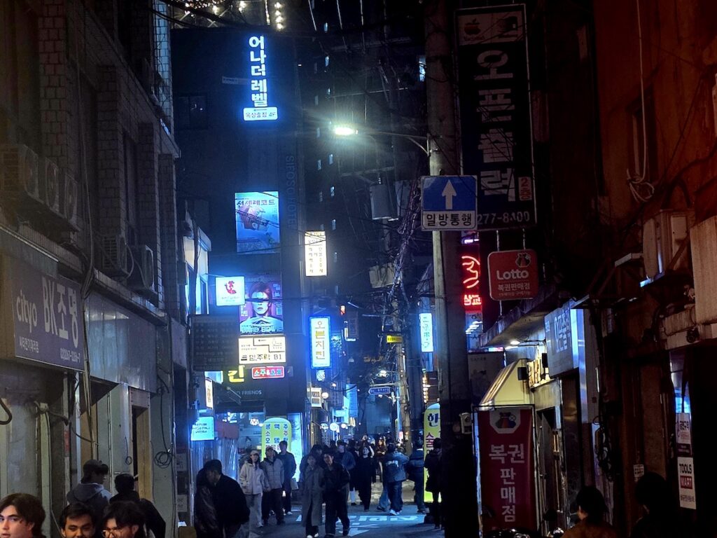 is-seoul-safe-from-pickpockets-hongdae-night-street Is Seoul safe from pickpockets image showing a busy Hongdae-style night street with neon signs and people walking through narrow alleys