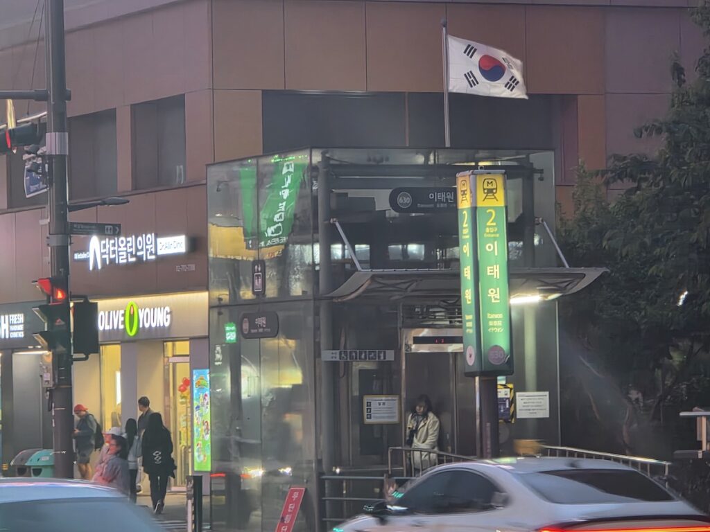 itaewon-seoul-station-exit-2-night Itaewon Seoul Station Exit 2 at night with shops, traffic, and Korean flag near the subway entrance