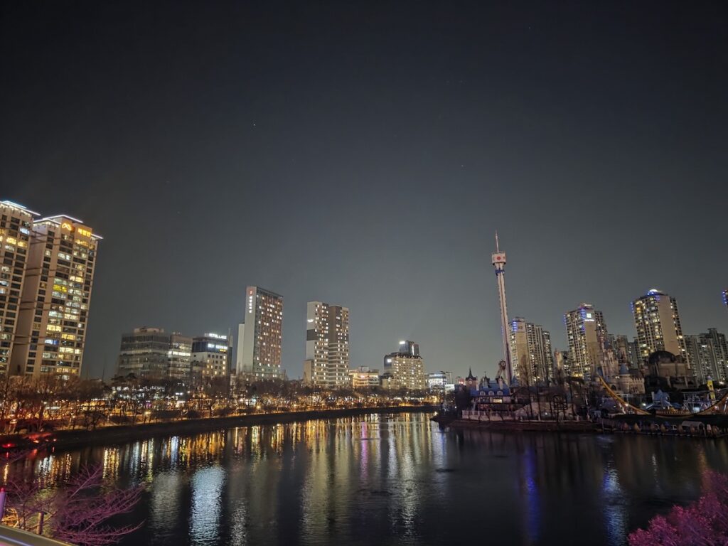 A scenic night view of residential apartments in Jamsil reflecting on Seokchon Lake, showcasing the authentic **Jamsil Local Life**.