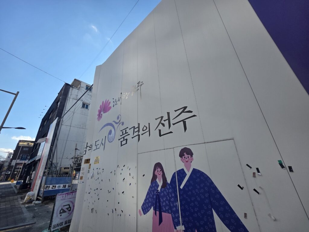 jeonju-cultural-mural-hanbok-welcome A street mural in Jeonju featuring an illustration of a couple in traditional Hanbok and the calligraphy "City of Dignity, Jeonju," welcoming international visitors.