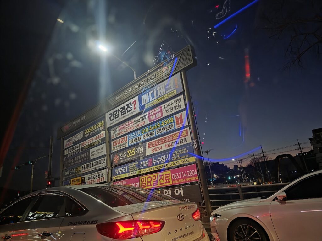 A dense collection of medical and service billboards illuminating the road during Jeonju night scenes.