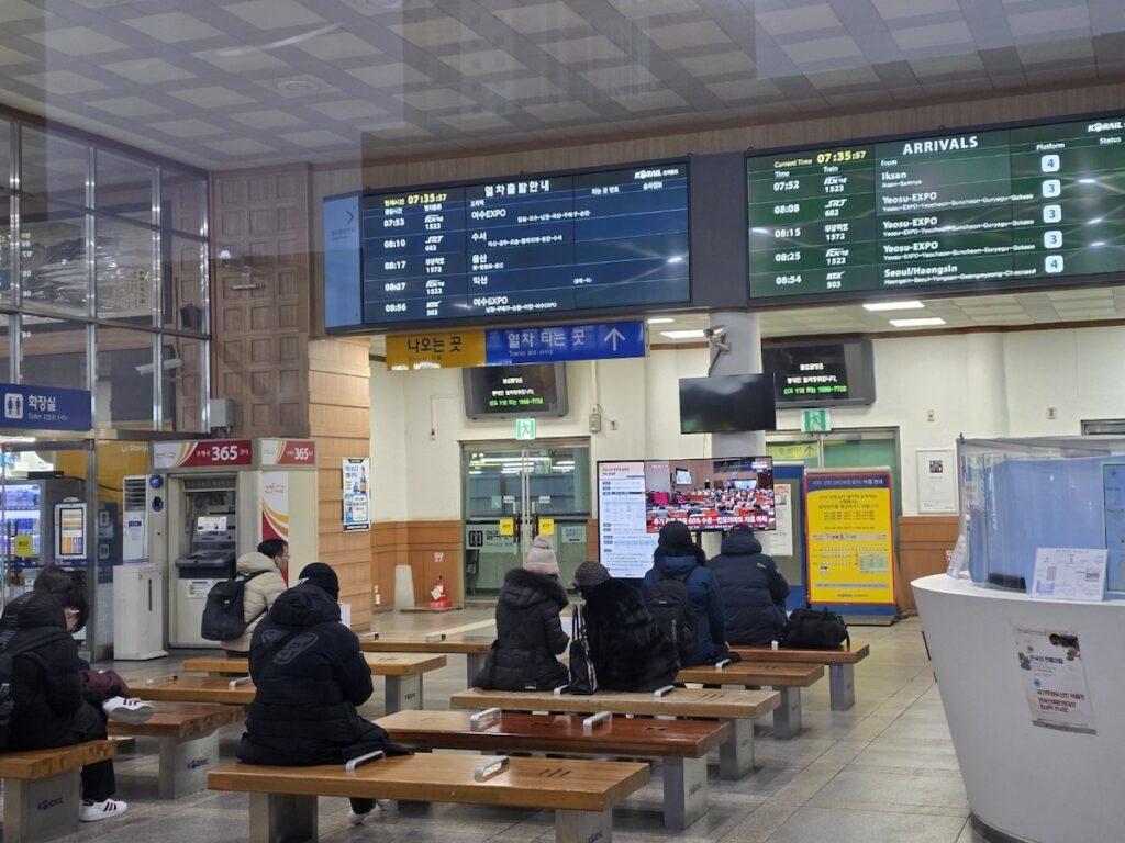 A busy waiting area at Jeonju Station with electronic boards showing the tight SRT and KTX departure schedules.