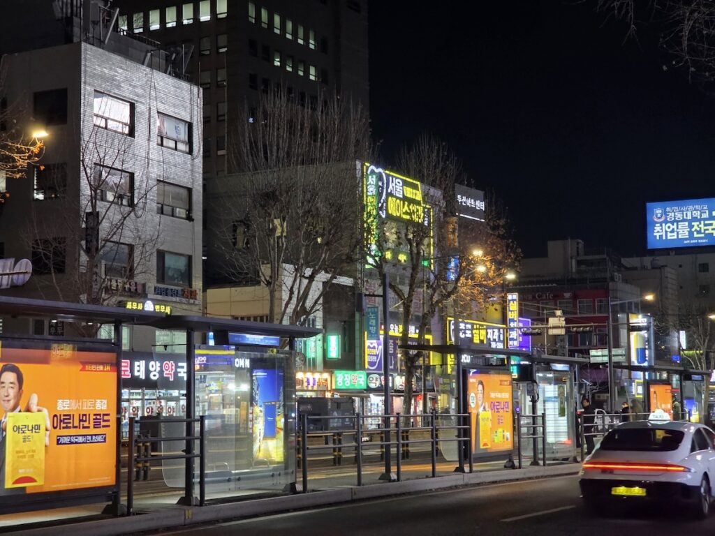 A cinematic night view of Jongno 5-ga Pharmacy Street with bright pharmacy signs and city traffic, showcasing the massive scale of Seoul's medical district.