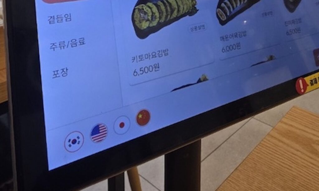 kiosk-language-selection-english-chinese-japanese A close-up of the language selection icons (USA, China, Japan flags) on a **Self-Service Kiosk in Korea**, highlighting ease of use for foreigners.