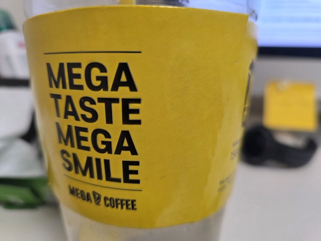 A close-up of a Mega MGC Coffee cup with the "Mega Taste Mega Smile" slogan, showcasing authentic Korea Coffee Brands.