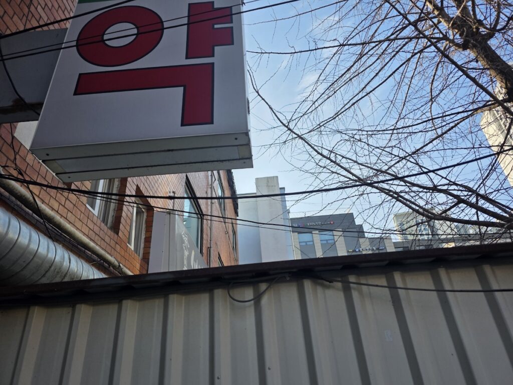 korea-pharmacy-guide-2026-red-sign A classic red and white Korean pharmacy sign hanging on a brick building, a key visual for the Korea Pharmacy Guide 2026.