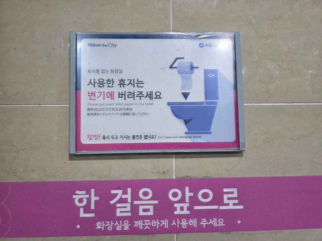 A standard Seoul subway bathroom sign in Korean, English, Chinese, and Japanese, explaining the Korea toilet etiquette of flushing paper.