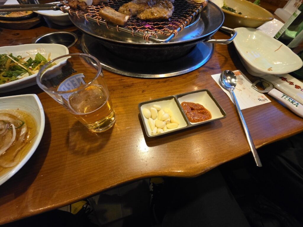 korean-bbq-sauce-garlic-ssamjang Essential Korean BBQ condiments: whole raw garlic cloves and savory Ssamjang dipping sauce on a wooden restaurant table.