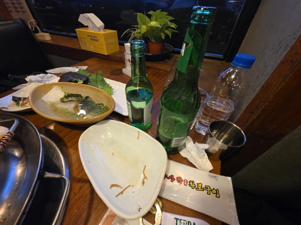 korean-bbq-table-setting-soju-beer A full Korean BBQ table setup featuring bottles of Soju and Terra beer alongside refreshing water kimchi and side dishes.