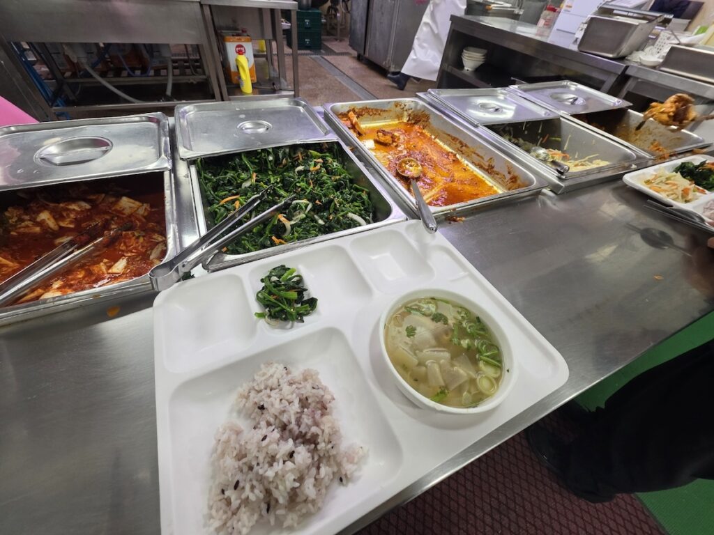 A complete 6,000 KRW Korean company cafeteria meal featuring black rice, soup, and various side dishes.