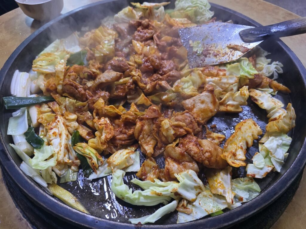 korean-dakgalbi-stir-fried-chicken A sizzling pan of Korean Dakgalbi (spicy stir-fried chicken) with cabbage and rice cakes, perfect for making lettuce wraps.
