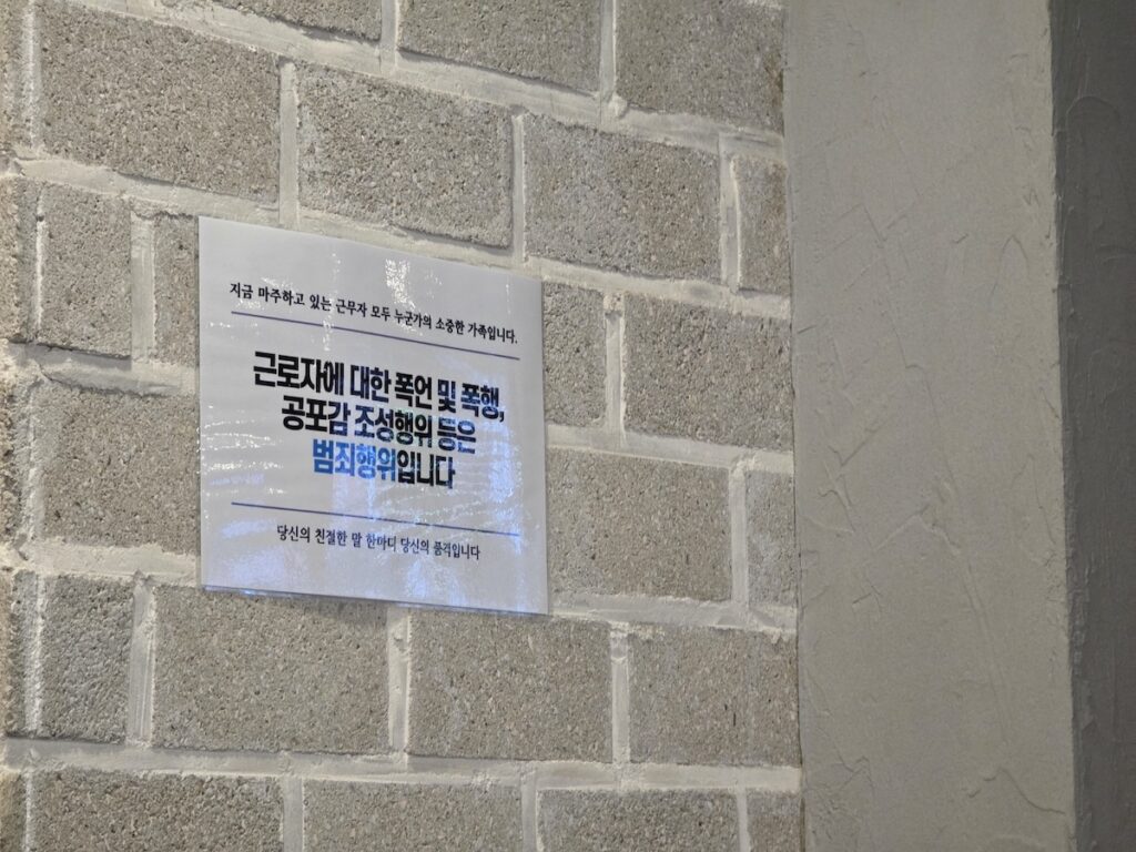 korean-dining-experience-worker-protection-notice A warning sign on a brick wall during a Korean Dining Experience stating that verbal abuse or violence against workers is a crime, reflecting the Occupational Safety and Health Act.