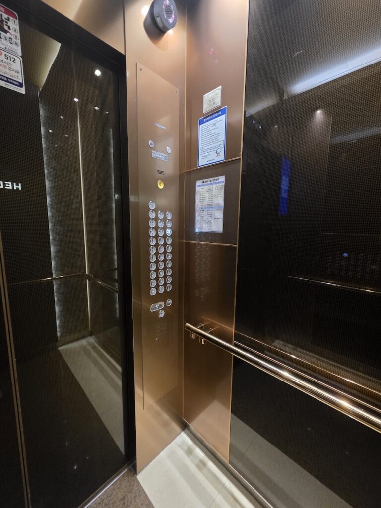 “Interior of a modern Korean elevator showing clean design and control panel with multiple floor buttons”
