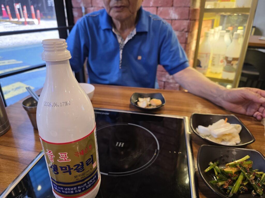 A Korean elder at a low table with a bottle of Julpo makgeolli, illustrating the everyday setting of the Korean hyung system