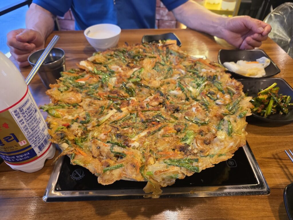 korean-hyung-system-haemul-pajeon-shared A large Korean seafood pancake shared between two people with makgeolli at a Korean restaurant table