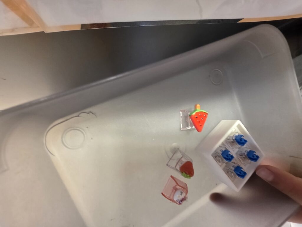 korean-keycap-keyring-components-tray A small shopping tray holding a 4-key acrylic base plate along with Hello Kitty, strawberry, and watermelon character keycaps.