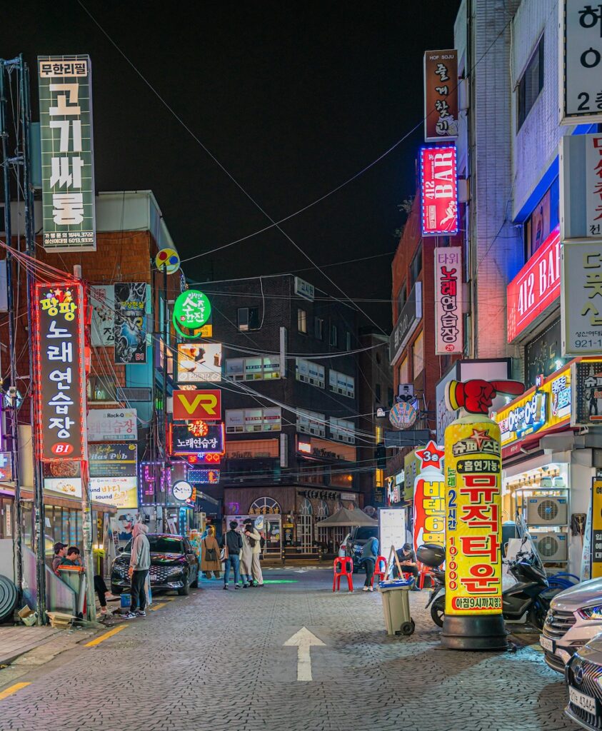 Neon lights and noraebang signs glowing on a Korean street at night, showing the nightlife atmosphere of Korea.