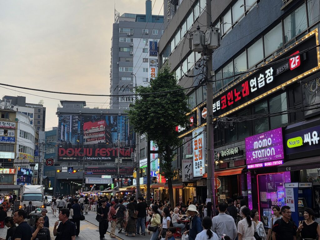 korean-outdoor-drinking-culture-jongno-street-dusk-atm Jongno street at dusk with neon signs, food stalls, and a 24-hour ATM, the setting for Korean outdoor drinking culture
