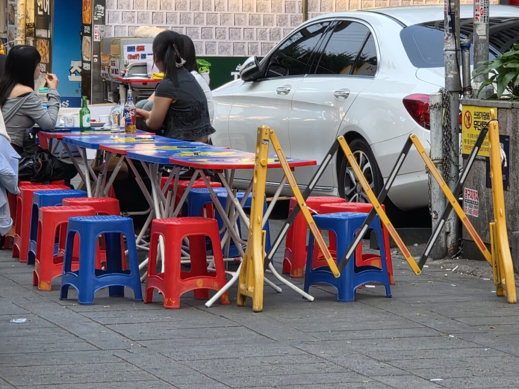 korean-outdoor-drinking-culture-pojangmacha-tents-dusk A row of pojangmacha tents beside a convenience store at dusk, part of Korean outdoor drinking culture