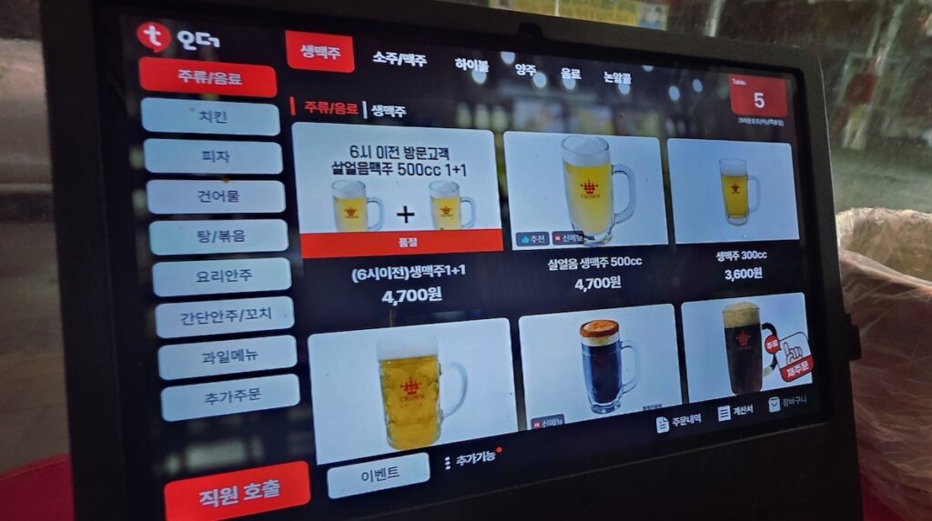 A table-top ordering system in a Korean pub showing draft beer options and a digital menu board for seamless ordering.