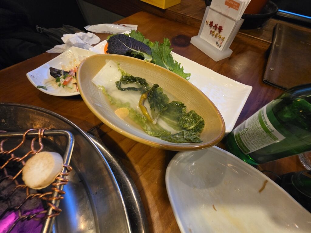 korean-side-dishes-dongchimi-water-kimchi Authentic Korean side dishes including refreshing Dongchimi (radish water kimchi) and fresh leafy vegetables for ssam wraps.