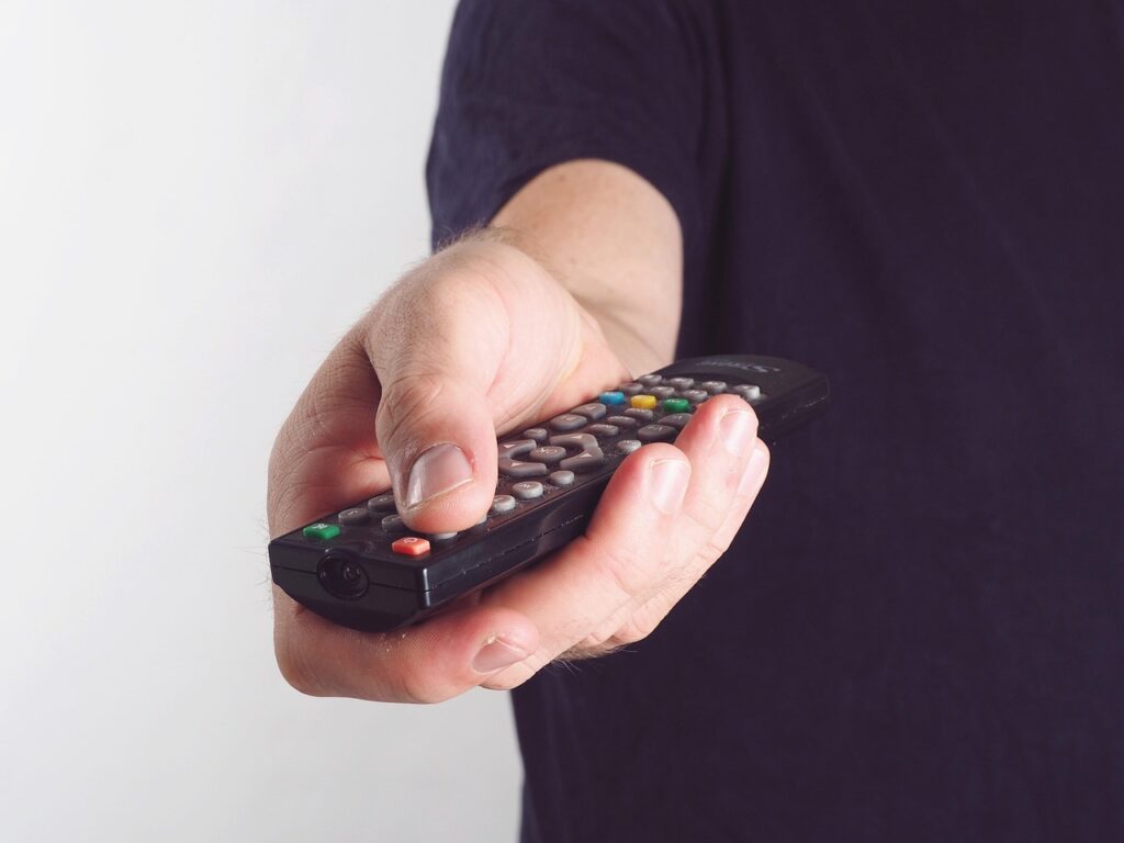 "A person holding a TV remote control while browsing Korean TV channels, representing how viewers access dramas, news, and variety shows in 2025."