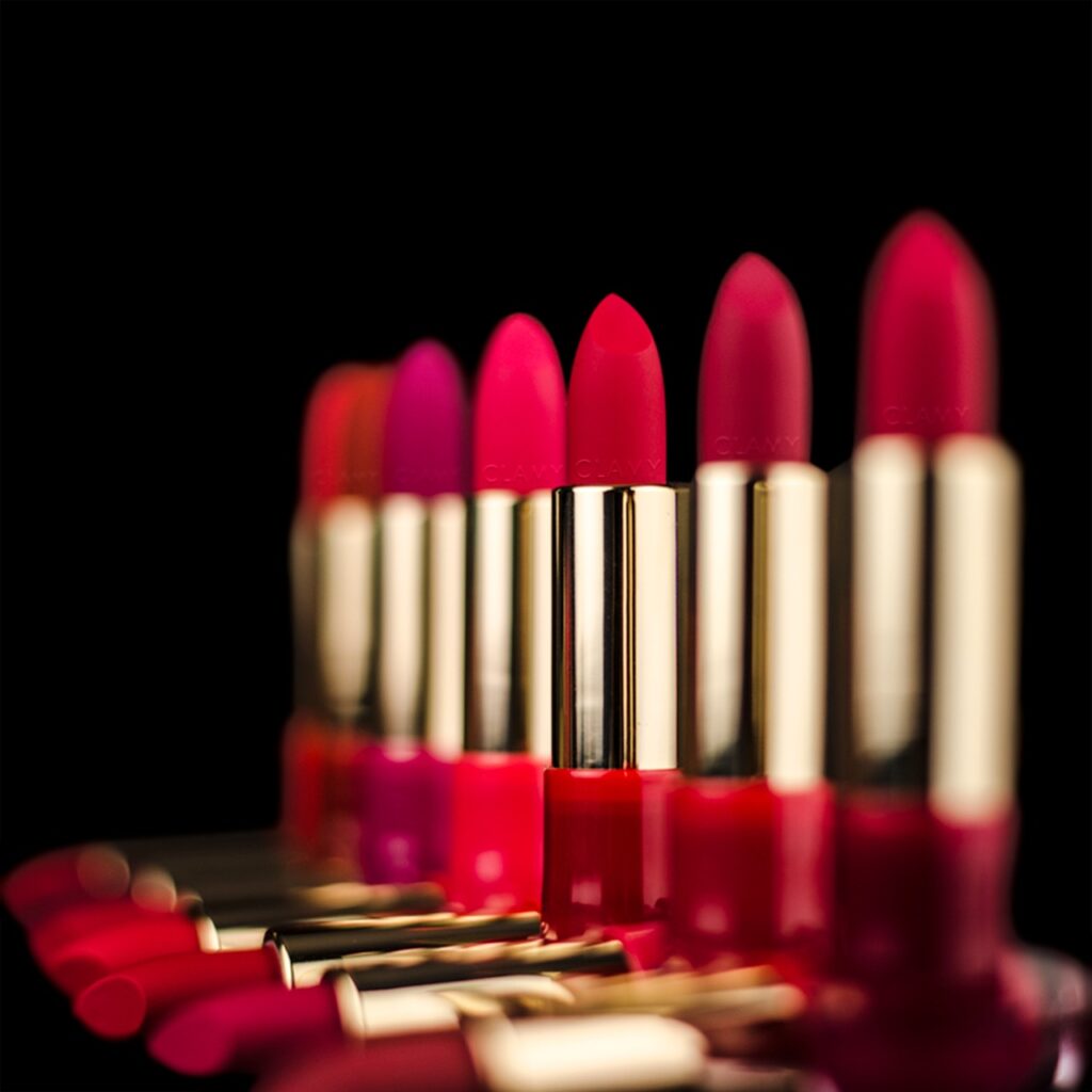 "A close-up of a woman applying red lipstick, contrasting the Korean soft gradient lip style with the bold full coverage look common in Western makeup."