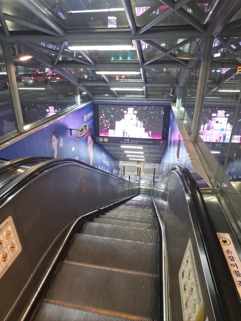 late-night-seoul-subway-station-entrance-tips Looking down the escalator of a quiet Seoul subway station late at night, a reminder to verify the Seoul subway and bus last call before entering.