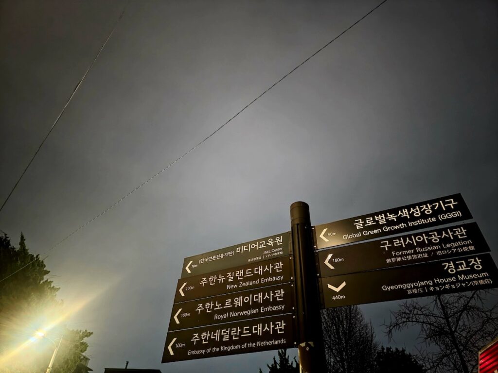 long-term-residency-korea-embassy-roadmap A cinematic night view of a signpost directing toward multiple global embassies in Seoul, symbolizing the complex journey of navigating F-2-99 visa Korea requirements.