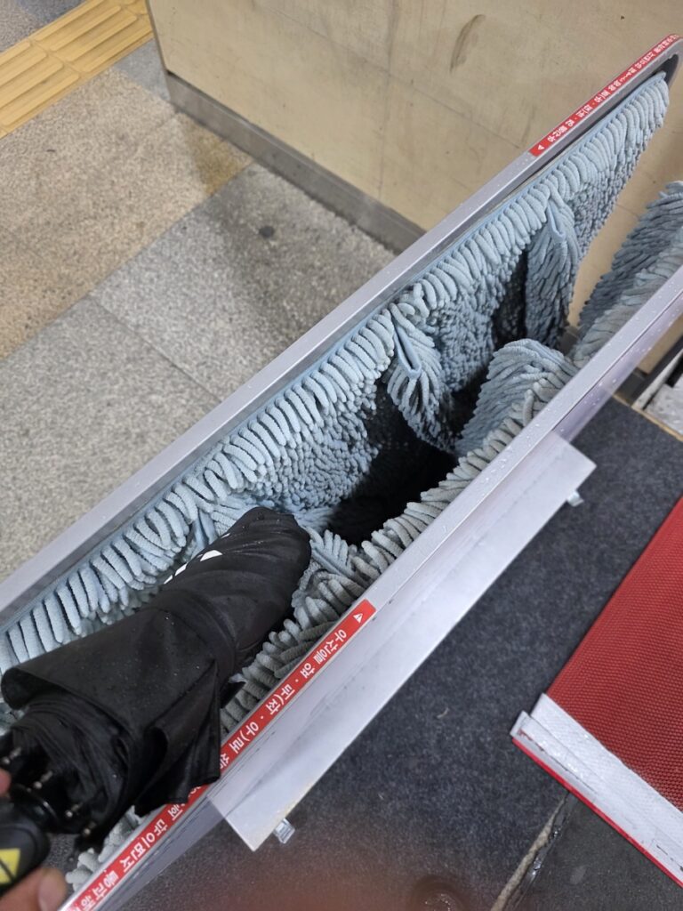 A manual umbrella wiper installed near a subway entrance in Seoul, used to remove rainwater from umbrellas.
