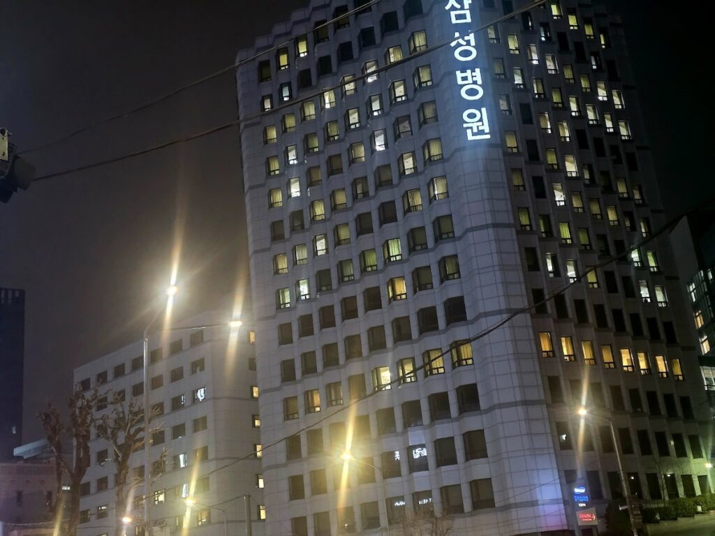 medical-emergency-korea-without-arc-seoul-healthcare-barriers A full view of a major hospital in Seoul at night with tangled power lines in the foreground, representing the complex administrative obstacles of a Medical Emergency Korea Without ARC.