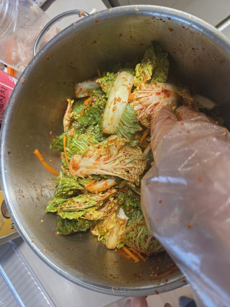 mixing-fresh-kimchi-salad-by-hand Hand-mixing fresh napa cabbage with spicy gochugaru seasoning, demonstrating the traditional way to keep the cabbage crunchy for high-fiber digestive health.