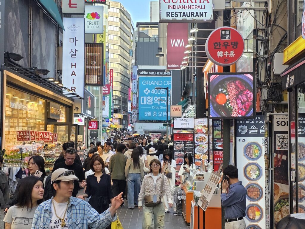 most-crowded-places-seoul-weekends-myeongdong-intersection-signs Busy Myeongdong intersection on weekend with large restaurant signs and crowds representing most crowded places in Seoul for tourists