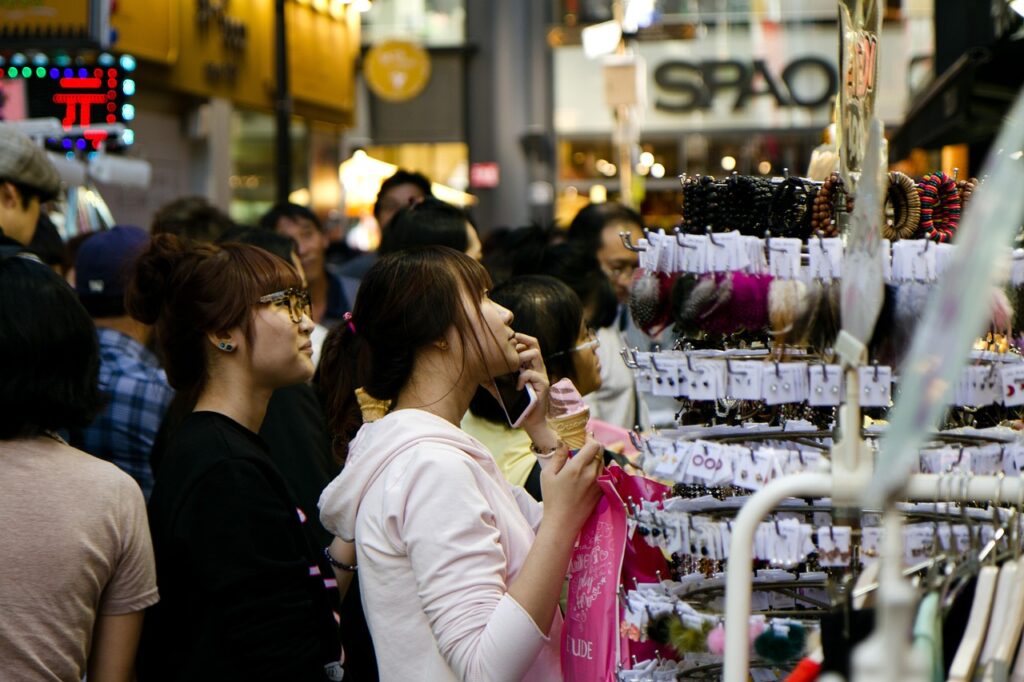 "Visitors walking along Myeongdong shopping street in Seoul at night, carrying shopping bags under bright neon signs and store lights."