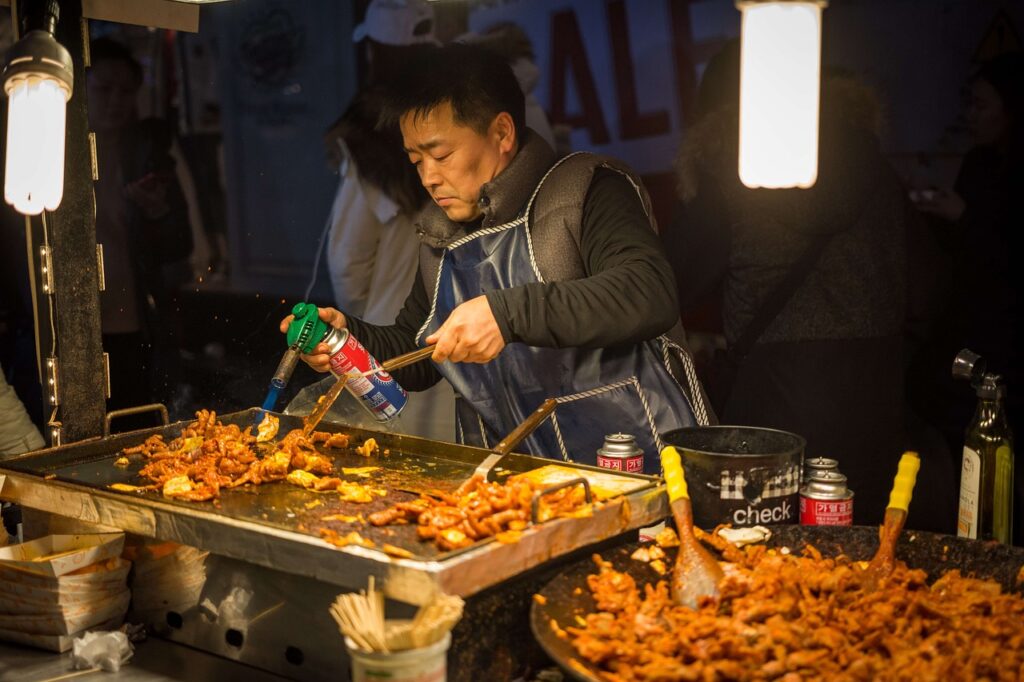 "Tourists enjoying Korean street food such as tteokbokki and hotteok from vendors in Myeongdong’s lively night market."