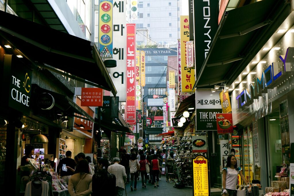 "Namdaemun Market in Seoul with locals and travelers walking through narrow alleys filled with street food stalls, fabric shops, and colorful signs."